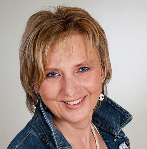 Frau mit kurzen blonden Haaren. Lächelt. Jeansbluse.