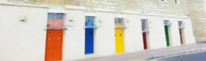 Eine weisse Häuserwand mit mehreren bunten Türen nebeneinander